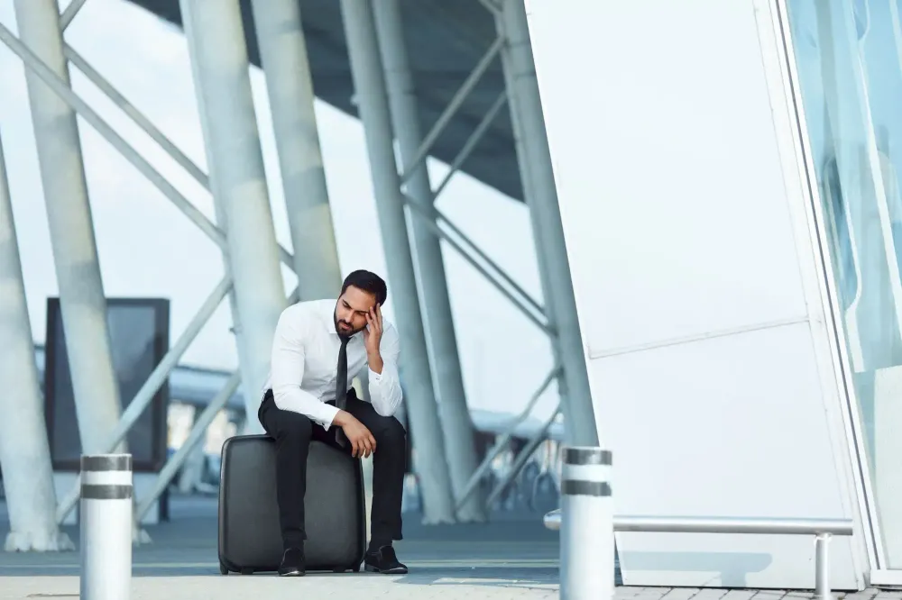 Distressed man sitting on his rolling suitcase at airport